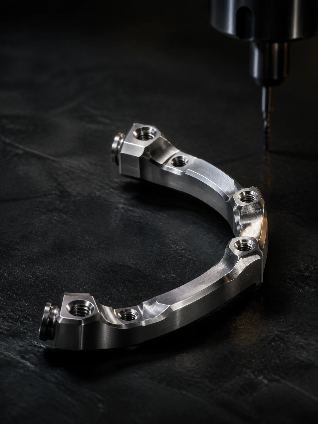 Machined titanium full-arch bar on a dark laboratory work surface